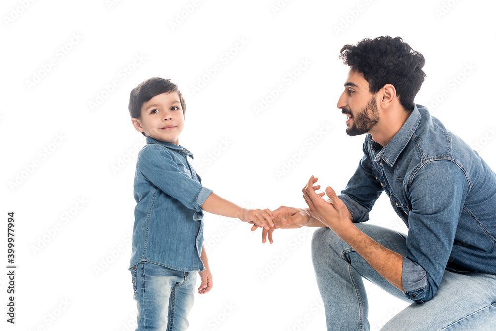 Smiling hispanic man holding hand of son isolated on white, two generations of men