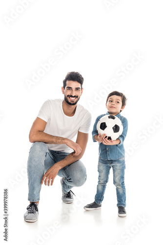 happy boy holding soccer ball near cheerful hispanic father isolated on white, two generations of men