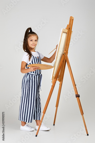 cute little girl holding a wooden art palette and brush on studio background. child painting. Full length