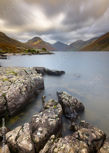 Jagged rocks on the shoreline of Wastwater with dramatic clouds and mountains in background. Lake District National Park, UK.