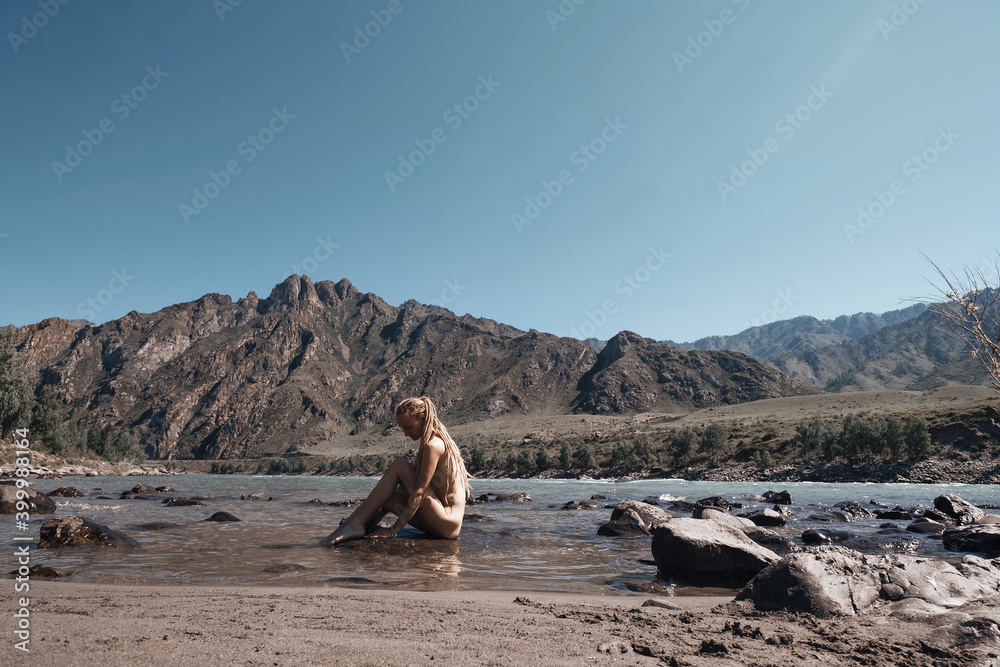Naked woman sitting on the stone of mountain river. Beautiful nature mountains landscape around