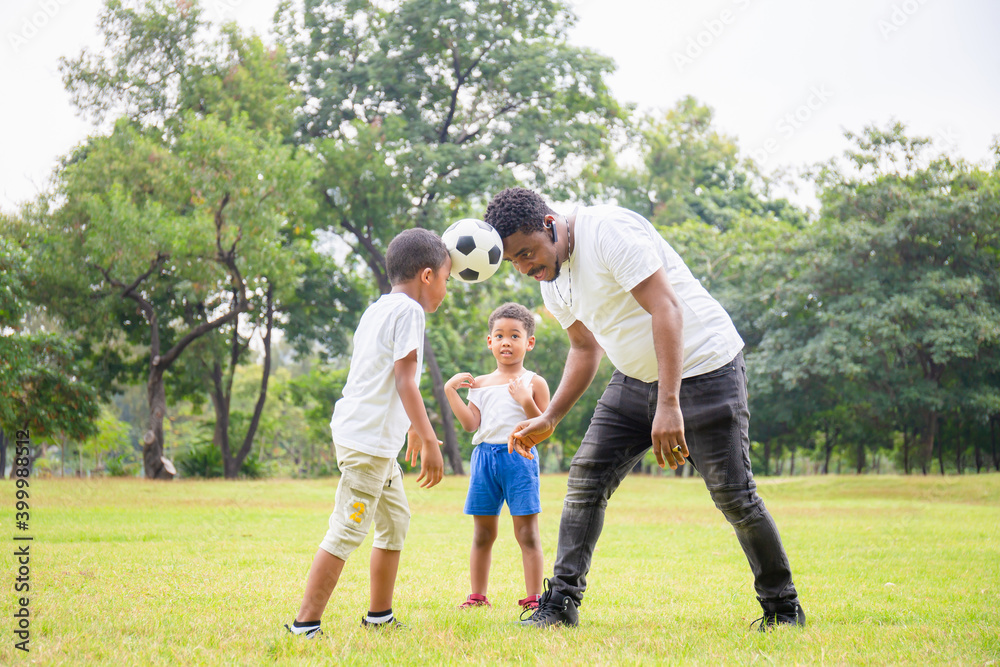 Cheerful african american father and two sons playing with football in park, Happiness family concepts
