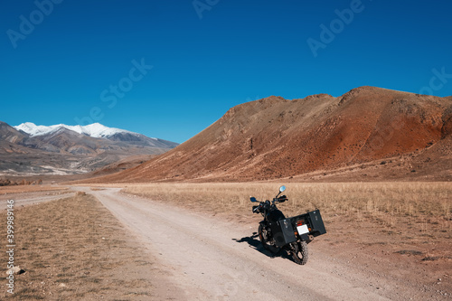 Motorcycle in mountains, red and snow mountain peaks on background. Off road moto travel in beautiful places