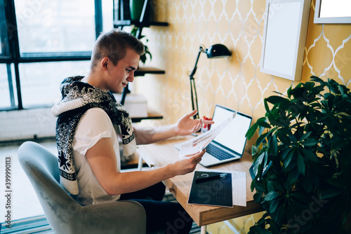 Freelance young handsome man checking work documents while using laptop in workplace at home photo