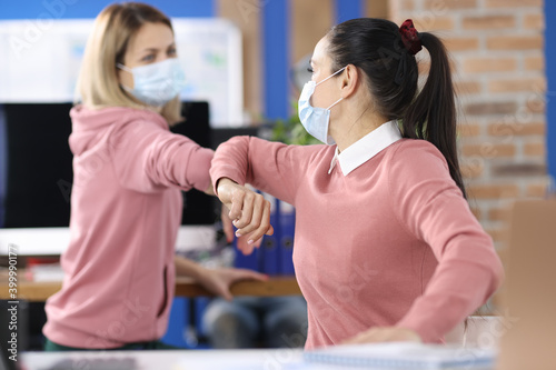 Two women in office in protective medical masks greet safely