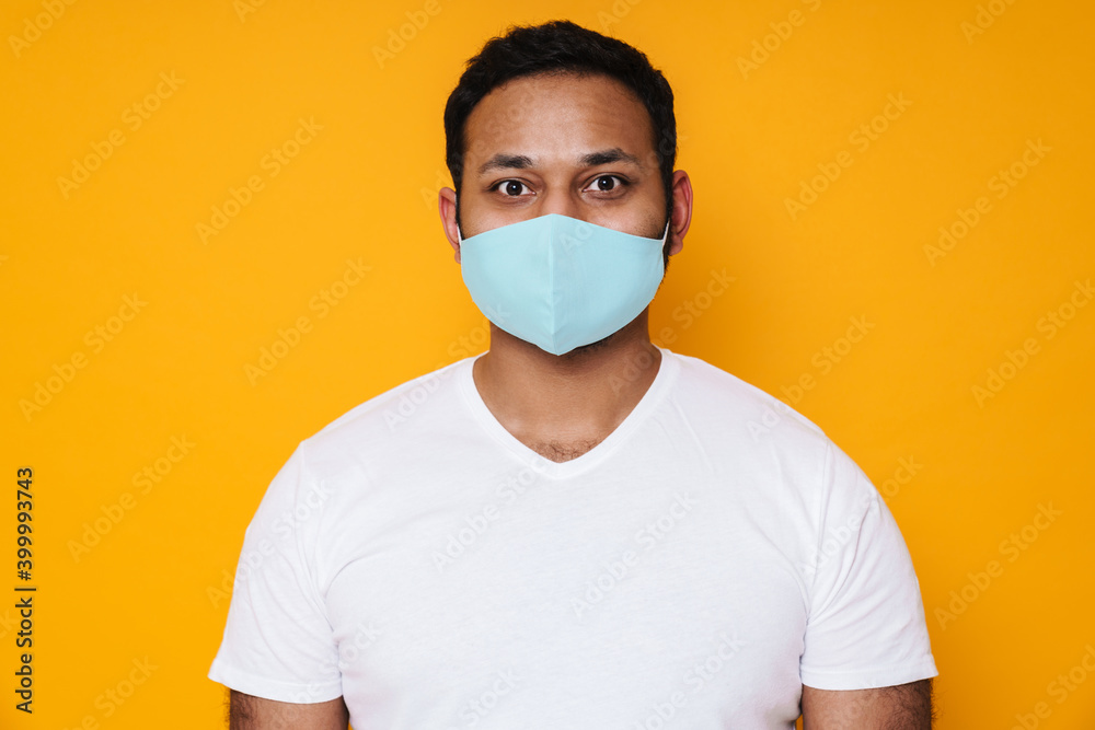 Asian brunette man in face mask posing and looking at camera isolated over yellow