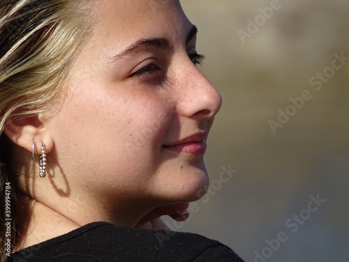 retrato rostro chica adolescente blanca con cabello castaño claro con mechones blancos con remera negra mirando hacia el costado, en un dia soleado photo