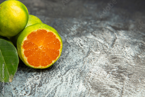 Fototapeta Naklejka Na Ścianę i Meble -  Half shot of of two fresh whole green tangerines with leaves and one cut in half tangerine on gray background footage