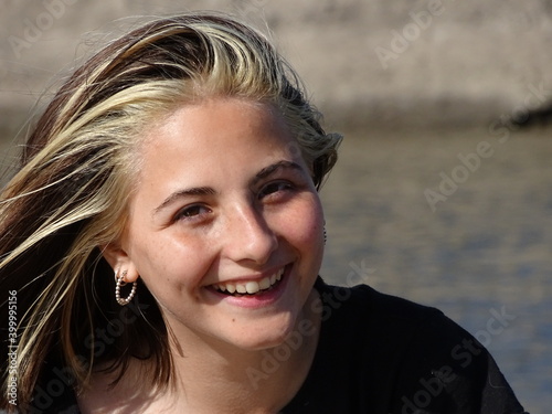 retrato rostro chica adolescente blanca con cabello castaño claro con mechones blancos con remera negra mirando la cámara y sonriendo, en un dia soleado photo