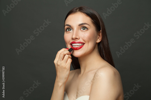 Nice woman applying lipstick makeup on lips on black background