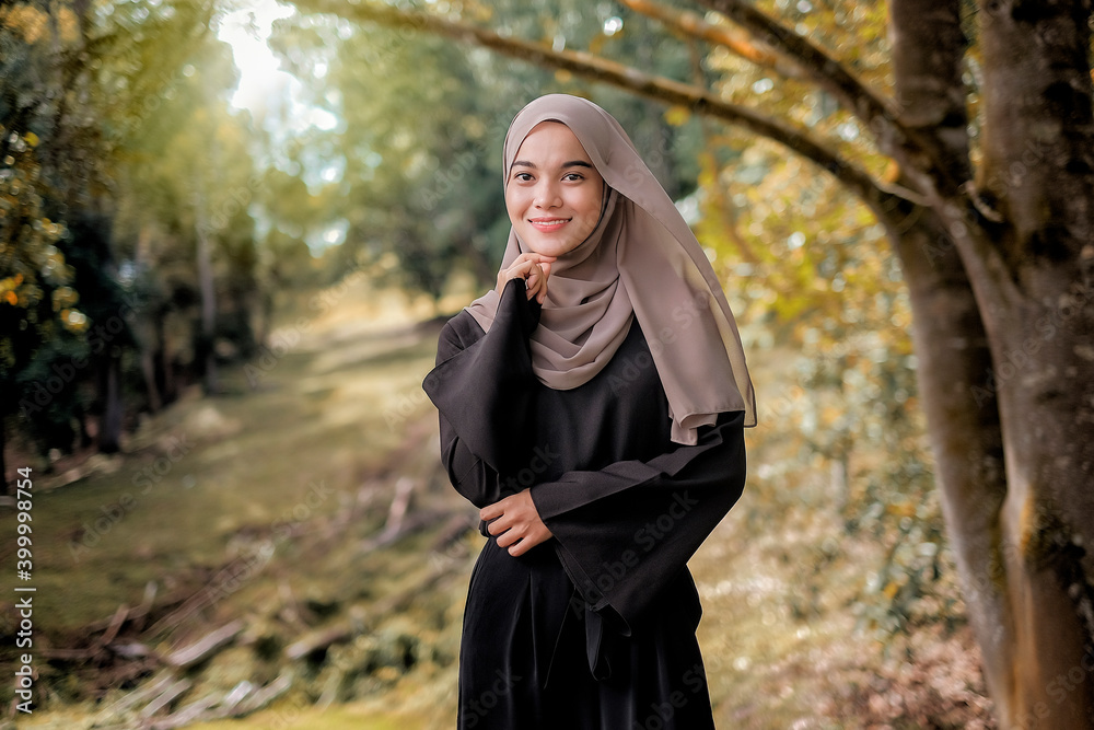 Beautiful and happy young moslem woman standing at the park in a sunny day with the green grass.