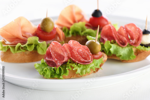 Tender baguette canapes with Leaf lettuce, salami or Parma ham, tomatoes, mozzarella and olive. Delicacy assorted platter for at the party.