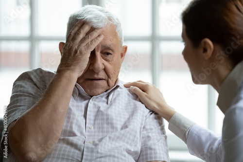 Attentive young lady physician interview senior patient on meeting listen to complaints make diagnosis. Stressed sad elderly man visit trusted capable doctor feel headache dizzy problems with memory photo