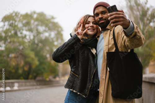 Multinational couple gesturing peace sign while taking selfie on cellphone
