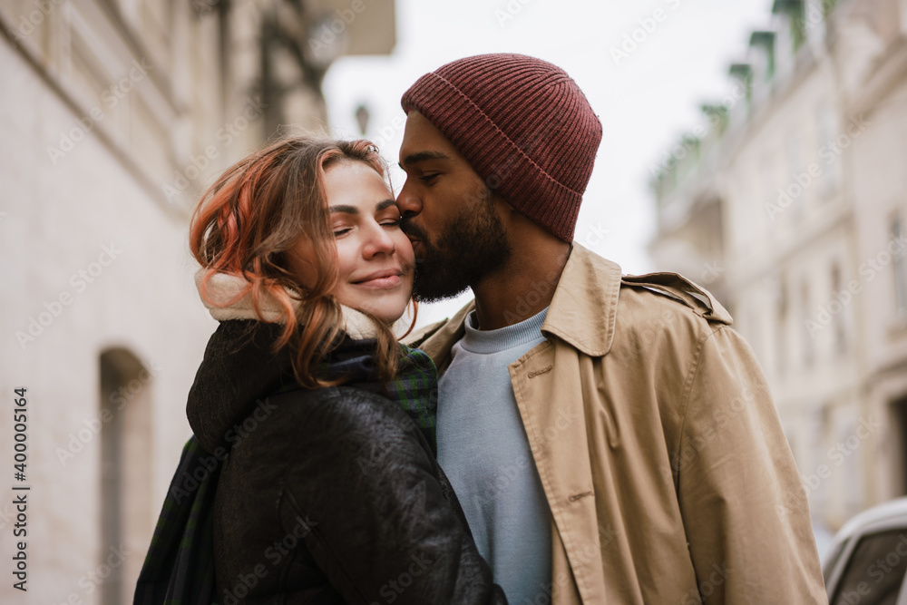 Naklejka premium Multinational beautiful happy couple smiling and kissing at city street