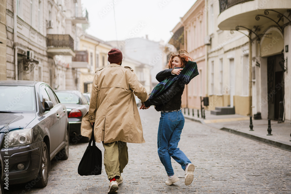 Multinational couple holding hands together and smiling while walking