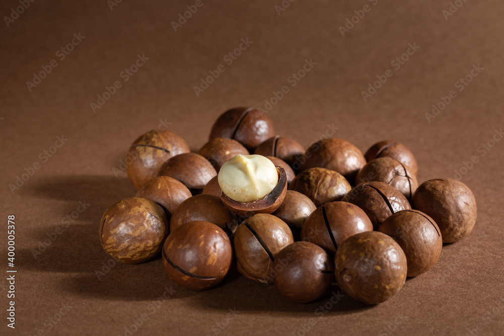 Obraz premium Heap of macadamia nuts on brown background. Copy space.