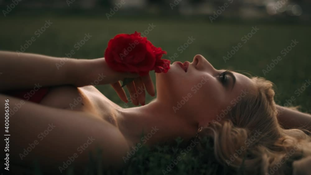 Fabulous girl with red lips in red dress on awesome summer roses background. Fantasy woman portrait. Awesome blonde model expresses emotions. Luxury lady in red is flirting. Beauty and style concept