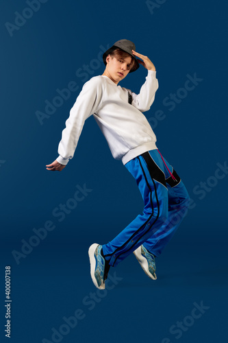 Balancing. Old-school fashioned young man dancing isolated on blue studio background. Artist fashion, motion and action concept, youth culture, fashion returning. Young caucasian curly boy.