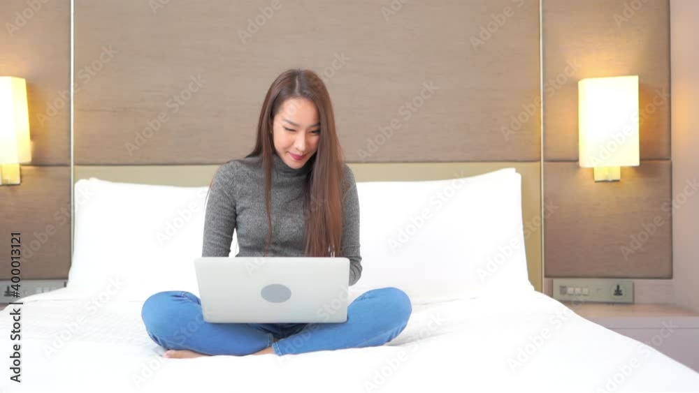 A pretty young woman enjoys sitting on the bed while working on her laptop. A pretty young woman enjoys sitting on the bed while working on her laptop.