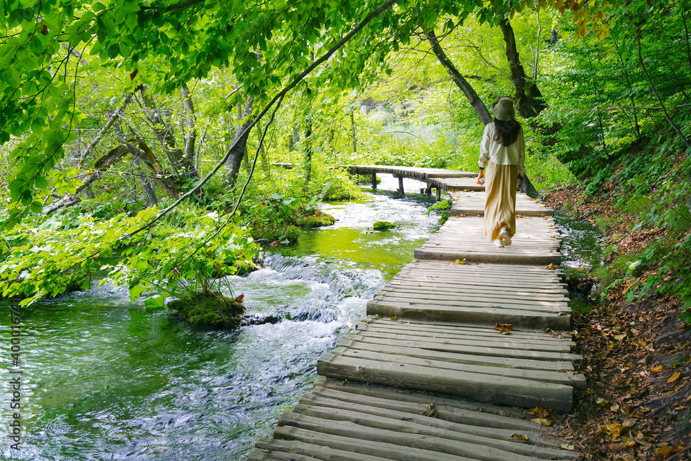 Fototapeta premium Young woman traveler walking on wooden path trail in Plitvice Lakes National Park, UNESCO natural world heritage and famous travel destination of Croatia
