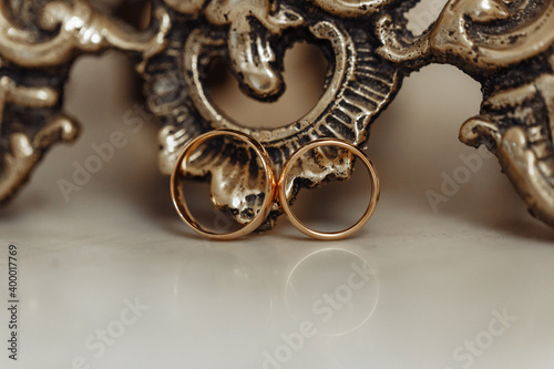 Two gold wedding rings, against the background of a bronze candlestick base. Close-up