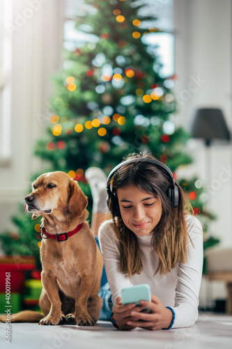 a girl with headphones lying in front of a Christmas tree with her dog
