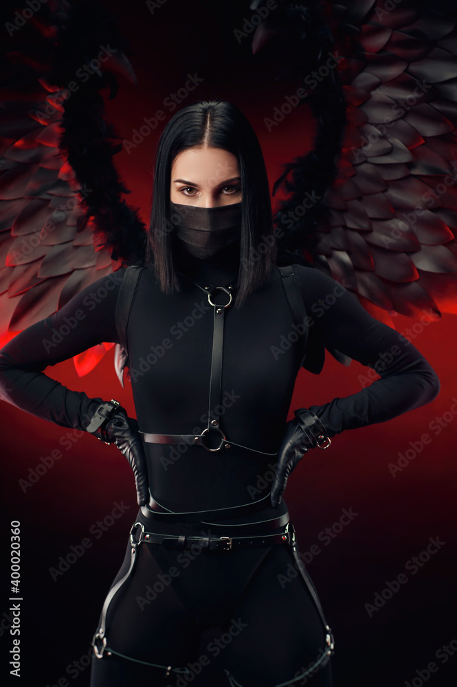a woman in a black bodysuit with leather straps and black wings on a dark red background
