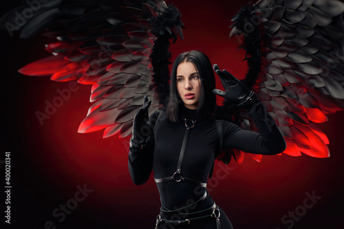 a woman in a black bodysuit with leather straps and black wings on a dark red background photo