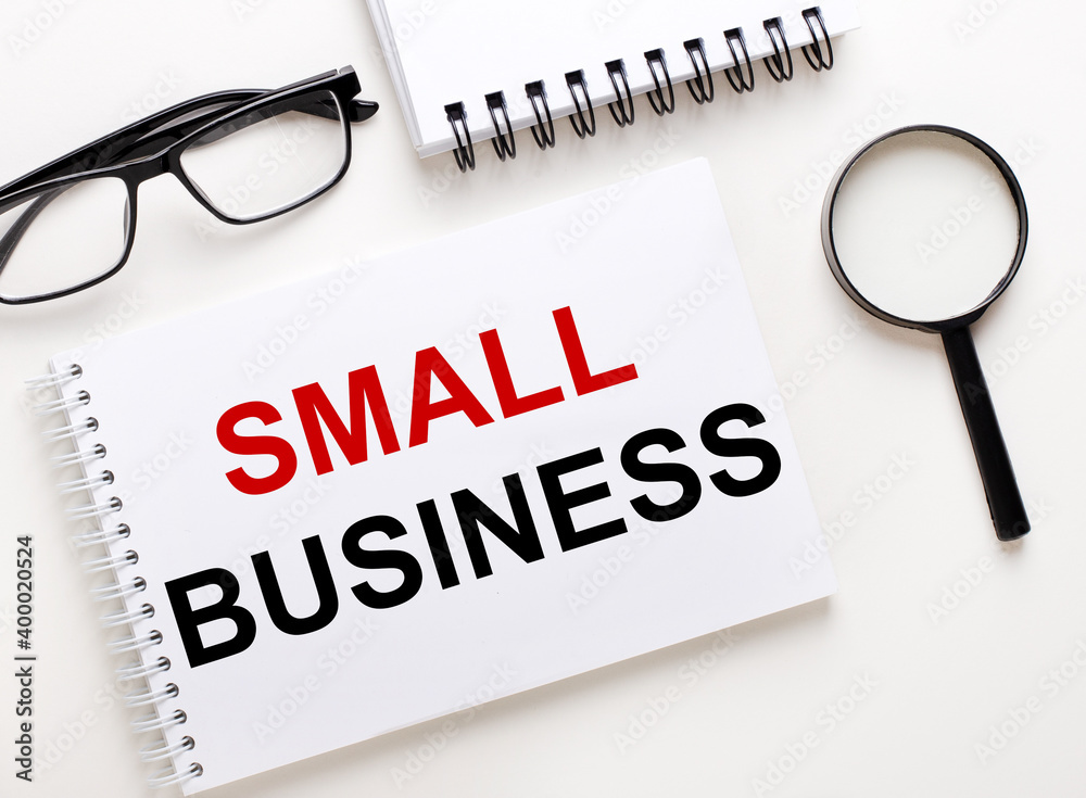 SMALL BUSINESS is written in a white notebook on a light background near the notebook, black-framed glasses and a magnifying glass. SMALL BUSINESS is written in a white notebook on a light background near the notebook, black-framed glasses and a magnifying glass.
