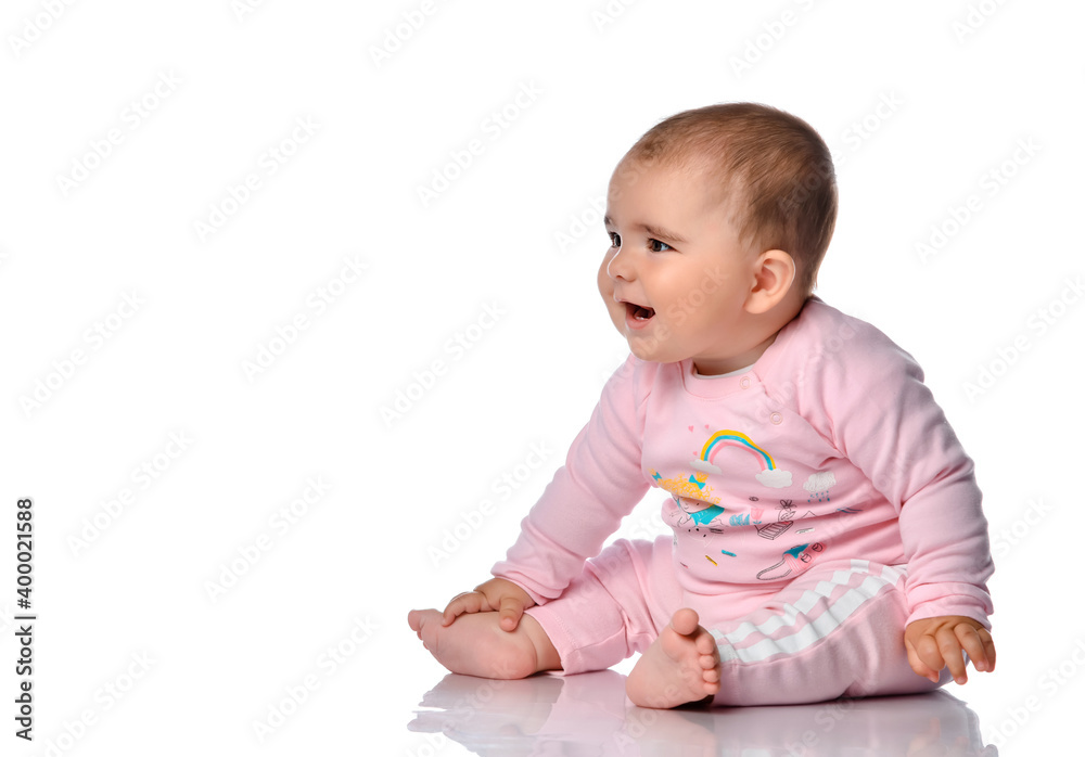 child sits sideways, looks to the side and smiles on a white background. Little beautiful cute barefoot girl dressed in pink clothes and looking at free space for text. child sits sideways, looks to the side and smiles on a white background. Little beautiful cute barefoot girl dressed in pink clothes and looking at free space for text.