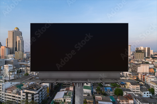 Blank black road billboard with Bangkok cityscape background at sunset. Street advertising poster, mock up, 3D rendering. Front view. The concept of marketing communication to promote or sell idea.