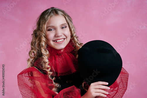 portrait of cute teenage girl. child in a black hat in a dress with red sleeves. retro style. pink background