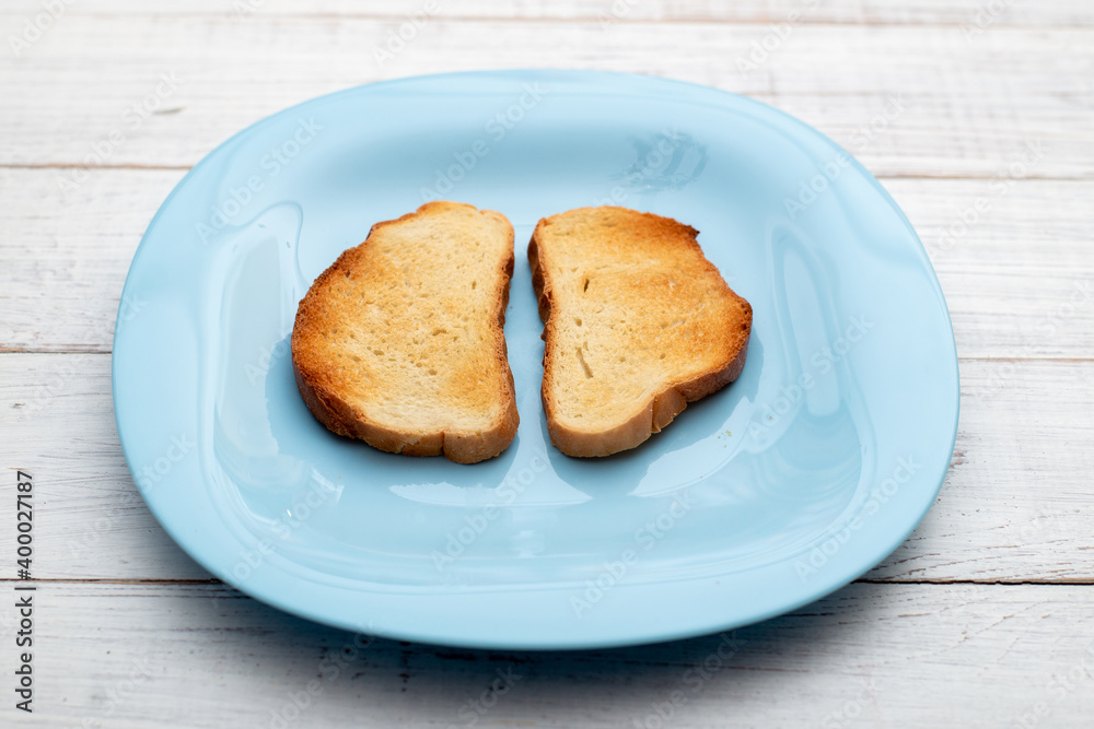 Toasted white bread on a blue plate on a white wooden background. Minimalism.