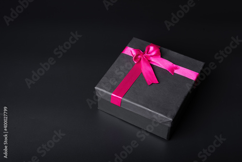 black gift box with red ribbon on dark black background and soft shadows
