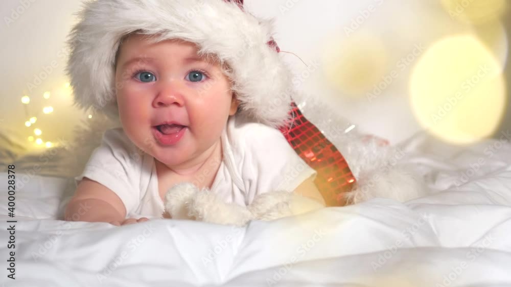 Adorable baby girl in Santa hat lying on white bed Adorable baby girl in Santa hat lying on white bed