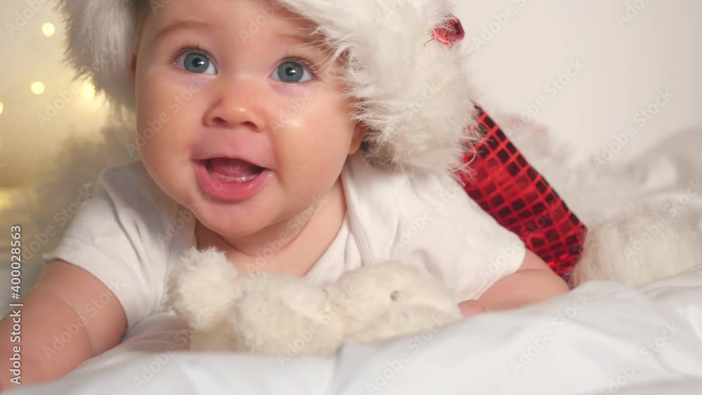 Adorable baby girl in Santa hat lying on white bed Adorable baby girl in Santa hat lying on white bed