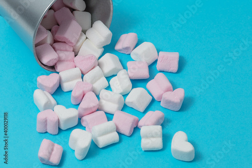 sweets-pink and white marshmallows in the shape of hearts fell out of a tin bucket on a blue background. Happy Valentine's Day. flat lay, copy space