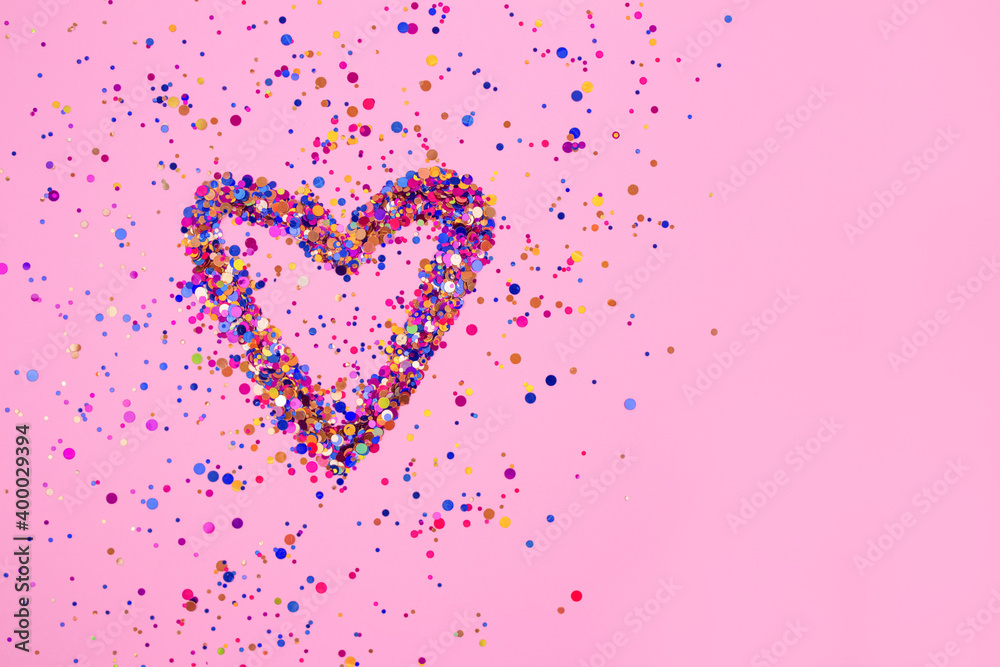 Heart made from explosion of shiny colorful sparkles on bright pink background with copyspace for your text. St. Valentine's day or birthday concept, selective focus