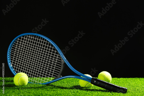 Tennis racket and balls on green grass against dark background. Space for text