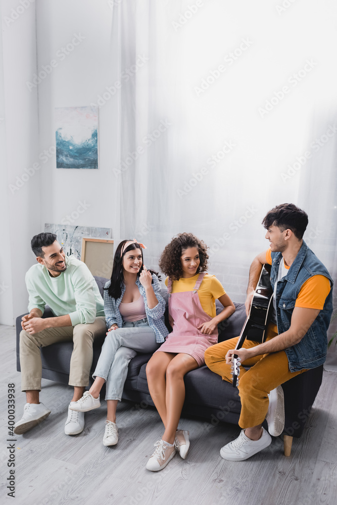 Fototapeta premium Smiling hispanic people looking at friends playing acoustic guitar at home
