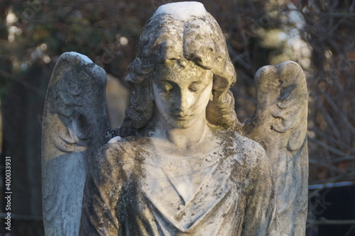 statue of a grieving marble angel covered in patina and snow on the grave