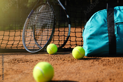 Tennis balls, rackets and bag near net on clay court