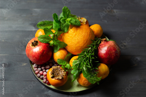 red and orange winter fruits  berries and greenery on plate on black background