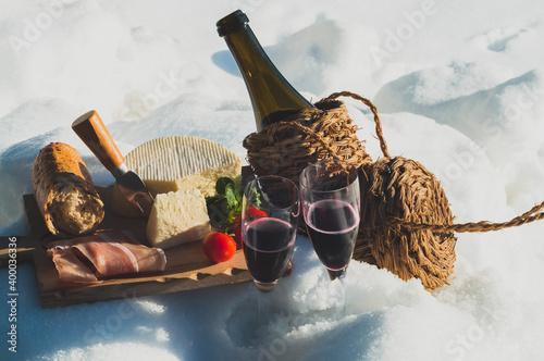 Romantic picnic with Lambrusco cheese baguette and ham on snow. Traditional Italian food and drink outdoor in sunny winter day.