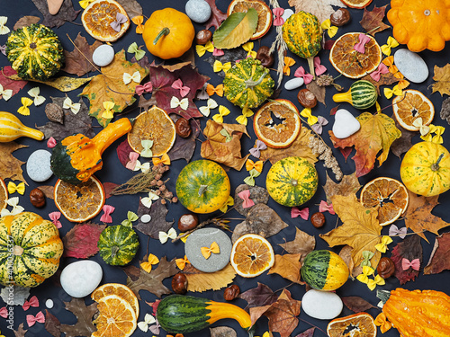 flat lay of autumn details - pumpkins, chestnuts, dried oranges, leaves, colored pasta bows, stones