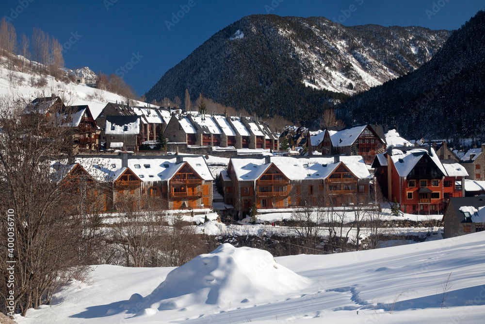 Panoramic view of some semi-attached mountain apartments for skiers, covered by snow on a sunny day in Salardú, Vall d’Aran, Lleida, Spain