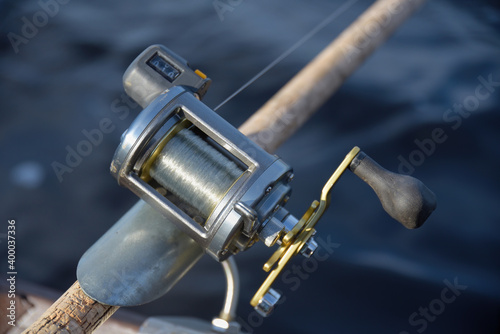 Round silver fishing reel with a line counter indicating almost 10 meters fishing line out place in a rod holder with blurred river water background. photo