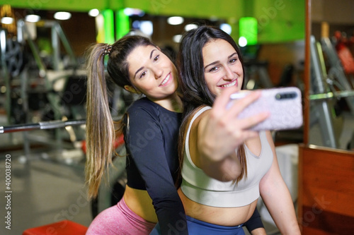 Portrait of two smiling sporty women taking a selfie photo in the gym. High quality photo