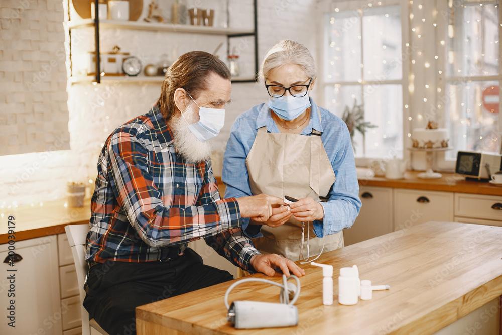 Fototapeta premium Old couple in a kitchen. Woman in a blue shirt and aprone. People in a medical masks.
